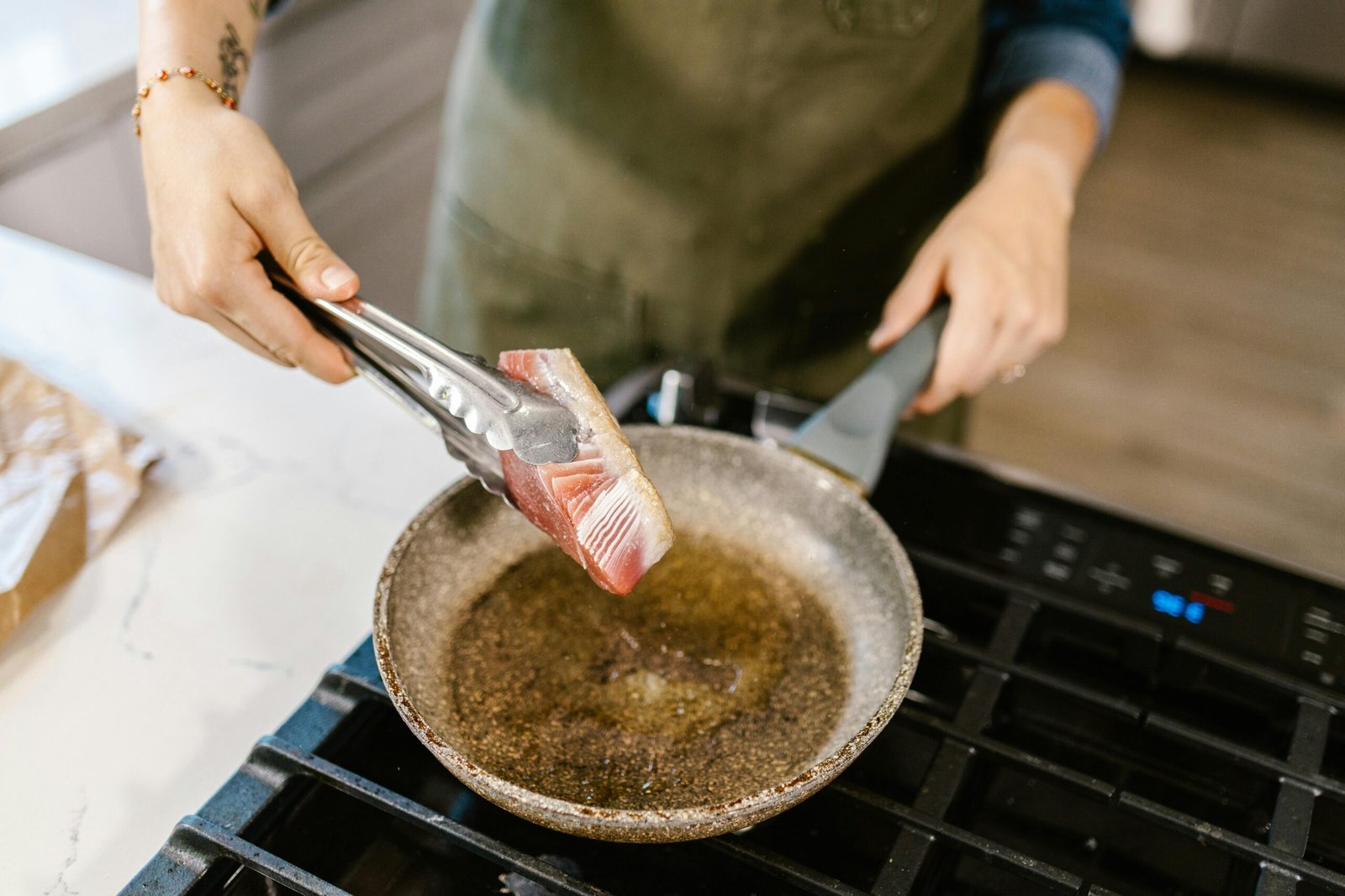 Person preparing fresh tuna steak in a frying pan using tongs.