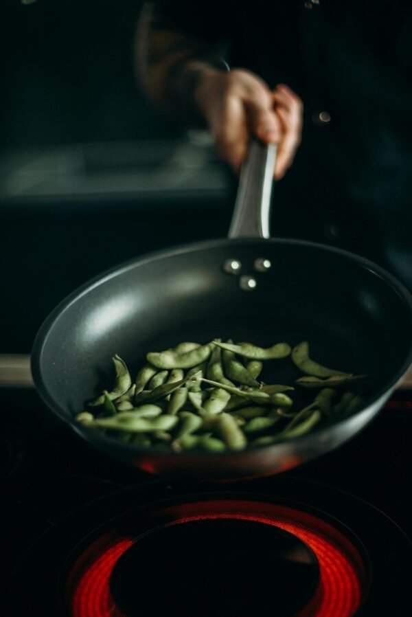 Close-up of edamame being cooked in a frying pan on an electric stove.